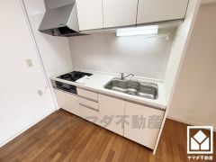 キッチンは空間を有効活用できる壁付けタイプ。明るい白色で統一された清潔感のあるデザインが魅力のシステムキッチンです。